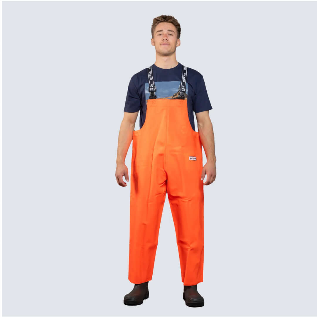 Salopette nautica OCEAN® arancione con bretelle nere, indossata su t-shirt navy, impermeabile da lavoro